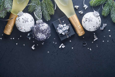 Christmas or New Year concept with black and silver baubles ball, gift box and champagne with decorated silver metallic ribbon on black background. Happy New Year 2022. Mock up.の写真素材