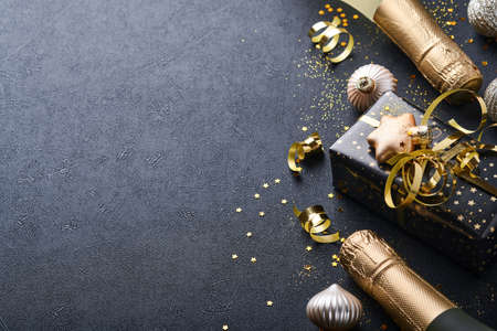 Christmas or New Year concept. Holiday gift box or present with ribbon, champagne, golden confetti and gold baubles on black background. Christmas card. Christmas Decoration. Mock up. Top view.の写真素材