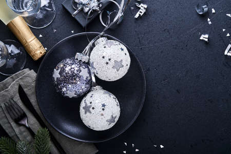 Christmas table setting black color with Christmas fir tree branches, Christmas silver balls and champagne, glasses on black background for xmas greetings. Merry Christmas and happy new year conceptの写真素材