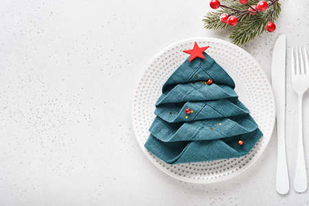 Christmas table setting white color with black silverware, napkin folded as a Christmas tree, Christmas silver balls, champagne, glasses on white background for xmas greetings. Empty space for text.の写真素材