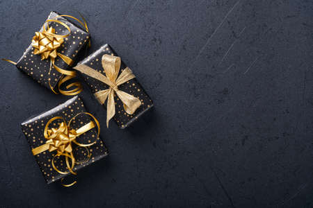 Holiday gift box or present with ribbon, golden confetti and gold baubles on black background. Magic christmas greeting card. Christmas Decoration. Border design. Mock up. Top view.の写真素材