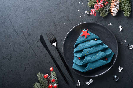 Christmas table setting black color with black silverware, napkin folded as a Christmas tree, Christmas silver balls, champagne, glasses on black background for xmas greetings. Empty space for text.の写真素材