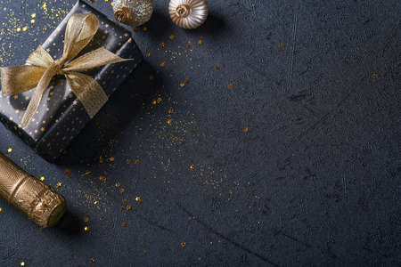 Holiday gift box or present with ribbon, golden confetti and gold baubles on black background. Magic christmas greeting card. Christmas Decoration. Border design. Mock up. Top view.の写真素材
