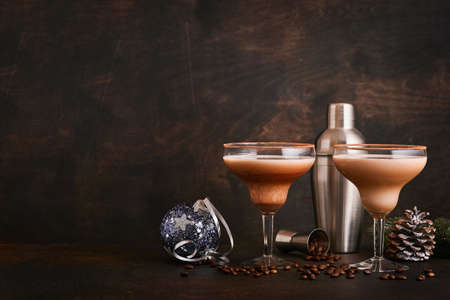 Alexander cocktail in cocktail glass on wooden table with shaker, nutmeg and small grater with Christmas decor on dark background. Beverage photography. Festive cocktail drink.の写真素材