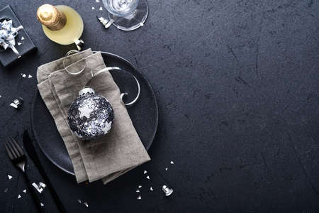 Christmas table setting black color with Christmas fir tree branches, Christmas silver balls and champagne, glasses on black background for xmas greetings. Merry Christmas and happy new year conceptの写真素材