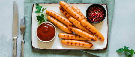 Grilled BBQ sausages with sauce and ketchup and garlic on ceramic plate on dark concrete background. Top view.の写真素材