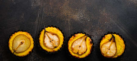 Pears and custard mini tarts on a dark brown concrete old table background. Top view.の写真素材