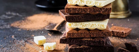 Mix stack of bitter, milky and white porous airy chocolate on dark old background. Selective focus.