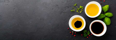 Soy sauce, olive oil and balsamic sauce with herbs basil, parsley, pepper and thyme in white ceramic bowls on black stone or concrete background.の写真素材