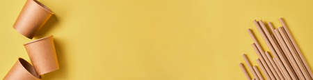 Brown paper drinking straws and eco paper glasses cornstarch, biodegradable material on yellow color background. Zero waste and plastic free concept. Top view. Banner.の写真素材