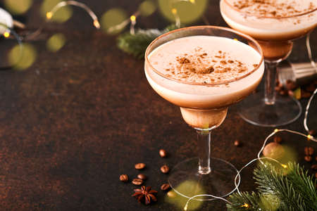 Alexander cocktail in cocktail glass on wooden table with shaker, nutmeg and small grater with Christmas decor on dark background. Beverage photography. Festive cocktail drink.の写真素材