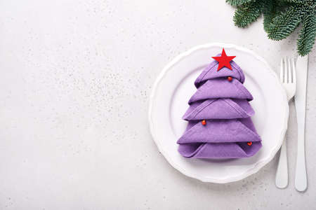 Christmas table setting white color with silverware, napkin folded as Christmas tree trendy color very peri in 2022 Year, Christmas balls, champagne, glasses on white background. Mock up.の写真素材