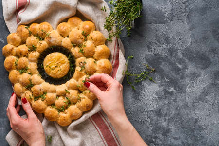 Female hands holding roasted camembert cheese and homemade bread heart shaped and thyme on rustic...