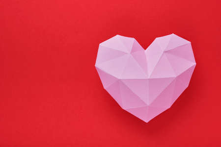 Pink paper heart isolated on red background. Red polygonal paper heart for Valentine's day or any other Love invitation cards. Top view, copy space.の写真素材