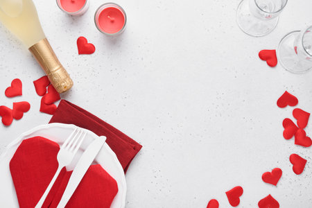 Valentinas day table setting white color with white silverware, red napkin folded as heart, candles, champagne, glasses on white background for greetings. Romantic dinner or menu concept. Mock up.の写真素材