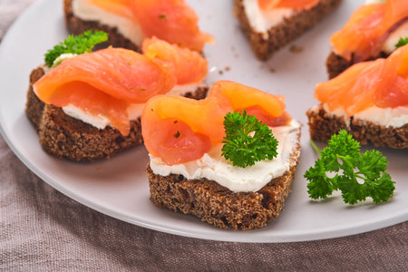 Mini sandwiches with salmon, curd cheese, parsley and rye bread in form of hearts. Valentine's day homemade creative food. Love breakfast design. Selective focus and copy spaceの写真素材