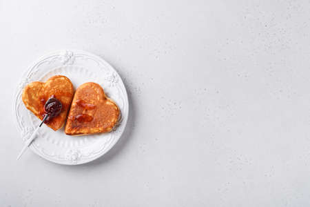 Two heart shaped pancakes with berry jam on white plate. Concept of festive breakfast for Valentines Day or pleasant surprise for loved one. Table viewed from above.の写真素材