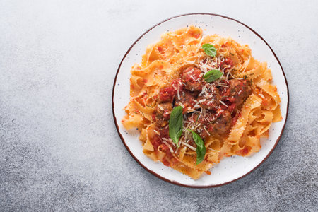 Tagliatelle pasta with meatballs in tomato sauce and thyme in sauce on light gray slate, stone or concrete background. Traditional Italian dish and cuisine. Top view with copy space.の写真素材
