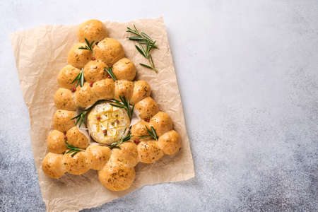 Bread buns Christmas tree with Roasted camembert cheese and rosemary on rustic background. Holiday...