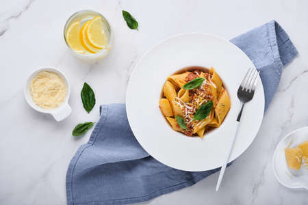 Bolognese Penne Pasta. Tasty appetizing classic italian penne pasta with parmesan cheese, basil and Bolognese sauce in white plate on stone table. Traditional dish of Italian cuisine. top view.の写真素材