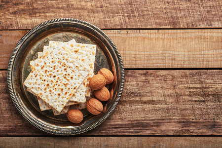 Matzah, red kosher and walnut metal tray. Traditional ritual Jewish bread on old wooden rustic background. Passover food. Pesach Jewish holiday of Passover celebration concept.の写真素材