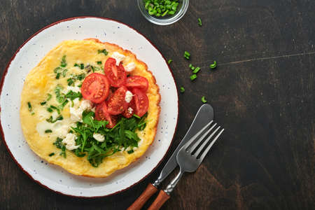 Rustic omelette or frittatas with green onions, cheese mozzarella, green arugula and tomatoes on old wooden dark background. Healthy food concept. Breakfast. copyspace. top view. Mock up.の写真素材