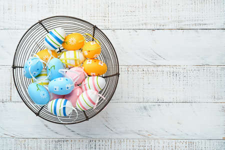 Easter holiday. Colorful Easter eggs in iron basket on white wooden background. easter greeting...