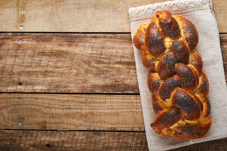 Shabbat Shalom. Bread challah with sesame seeds and poppy seeds on wooden background. Traditional jewish bread for Shabbat and Holidays. Rustic concept. Copy space. Selective focus.の写真素材