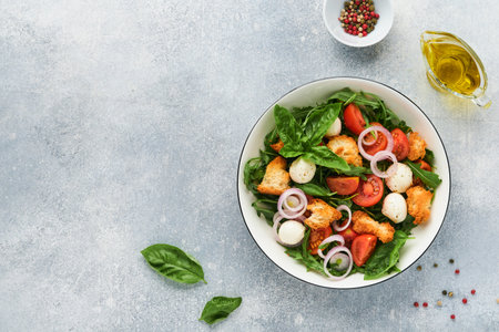 Panzanella, Italian Bread Salad. Traditional food of Italy with tomatoes, mozzarella balls, basil, onion and bread on light gray background. Traditional Italian cooking. top view. copyspace.の写真素材