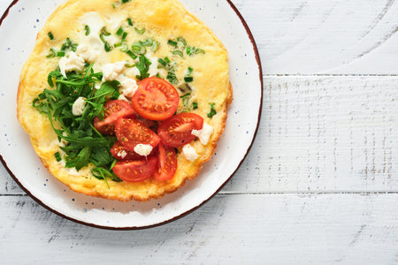 Rustic omelette or frittatas with green onions, cheese mozzarella, green arugula and tomatoes on old wooden white background. Healthy food concept. breakfast. copyspace. top view. Mock up.の写真素材