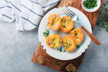 Egg muffins with green onions, bacon, cheese and tomatoes on white plate on light background....
