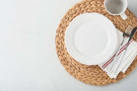Vintage zero waste silverware. Rustic vintage set of white plate, wooden spoon and fork on napkin for dishes from water hyacinth on light gray concrete background. empty dishes. top view. Mock up.の写真素材