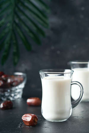 Ramadan Kareem food and drinks. Plate of dates, glass of milk and date palm branch on black background. Righteous Muslim Lifestyle. Vegetarian food. selective focus.の写真素材