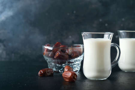 Ramadan Kareem food and drinks. Plate of dates, glass of milk and date palm branch on black background. Righteous Muslim Lifestyle. Vegetarian food. selective focus.の写真素材