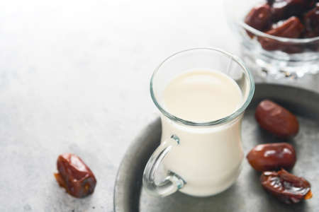 Ramadan Kareem food and drinks. Plate of dates, glass of milk and date palm branch on light gray background. Righteous Muslim Lifestyle. Place for text. selective focus.の写真素材