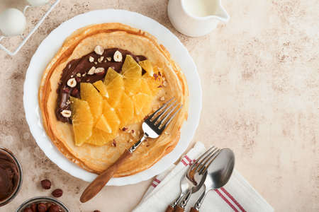 Crepes suzette with oranges. Thin crepes with chocolate spread, hazelnuts and orange slices fruit in white plate for breakfast on old concrete rustic table background. copyspace. top view.の写真素材