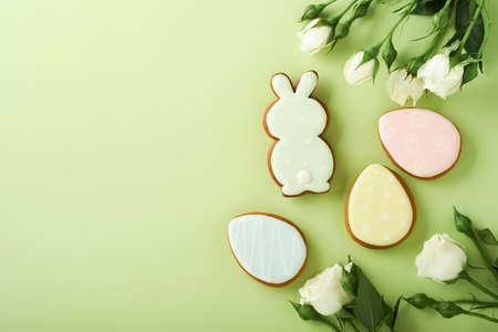 Happy Easter. Postcard with Easter cookies or gingerbread and beautiful flowers on light green background. Top view with space for your greetings.の写真素材