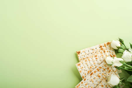 Passover celebration concept. Matzah, red kosher wine, walnut and spring beautiful rose flowers. Traditional ritual Jewish bread on light green background. Passover food. Pesach Jewish holiday.の写真素材