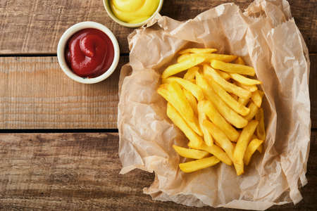french fries. Tasty French fries server on parchment paper on wooden cutting board with tomato and...