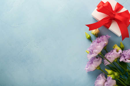 Festive flower composition purple color and gift box with ribbon on light blue concrete background. mothers day concept. flowers frame. overhead view. Top view with copy space.の写真素材