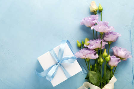 Festive flower composition purple color and gift box with ribbon on light blue concrete background. mothers day concept. flowers frame. overhead view. Top view with copy space.の写真素材