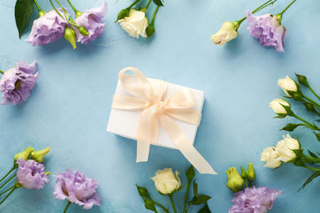 Festive flower composition purple color and gift box with ribbon on light blue concrete background. mothers day concept. flowers frame. overhead view. Top view with copy space.の写真素材