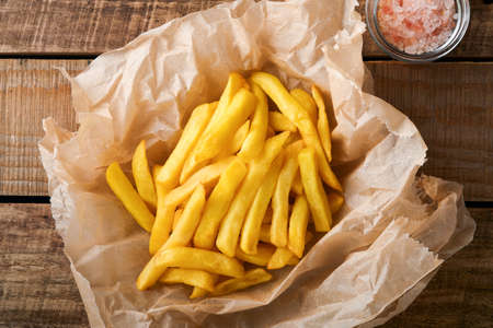 french fries. Tasty French fries server on parchment paper on wooden cutting board with tomato and cheese sauce on wooden table background. Diverse Keto Dishes. Fast food and unhealthy food concept.の写真素材
