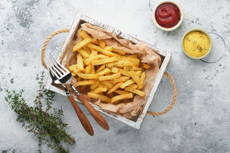 french fries. Tasty French fries server on parchment paper on wooden cutting board with tomato and...