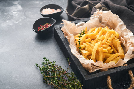 french fries. Tasty French fries server on parchment paper on wooden cutting board with tomato and cheese sauce on old black background. Diverse Keto Dishes. Fast food and unhealthy food concept.の写真素材