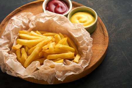 french fries. Tasty French fries server on parchment paper on wooden cutting board with tomato and cheese sauce on wooden table background. Diverse Keto Dishes. Fast food and unhealthy food concept.の写真素材
