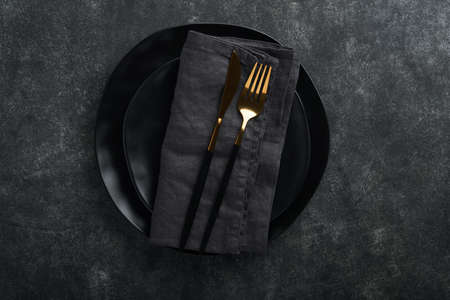 Ceramic empty black plate, silverware and linen kitchen towel napkin on old black ceramic cement...