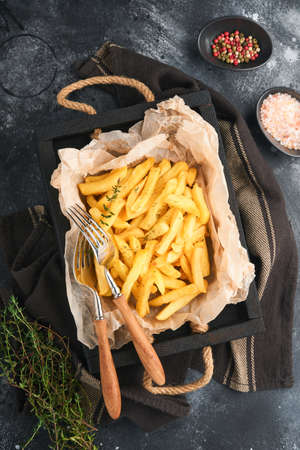 french fries. Tasty French fries server on parchment paper on wooden cutting board with tomato and cheese sauce on old black background. Diverse Keto Dishes. Fast food and unhealthy food concept.の写真素材