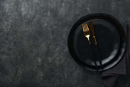 Ceramic empty black plate, silverware and linen kitchen towel napkin on old black ceramic cement...