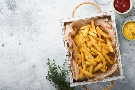 french fries. Tasty French fries server on parchment paper on wooden cutting board with tomato and...